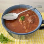 beef and barley stew in a mug on a yellow towel with a sprig of parsley