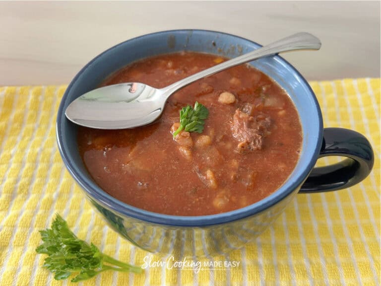 beef and barley stew in a mug on a yellow towel with a sprig of parsley