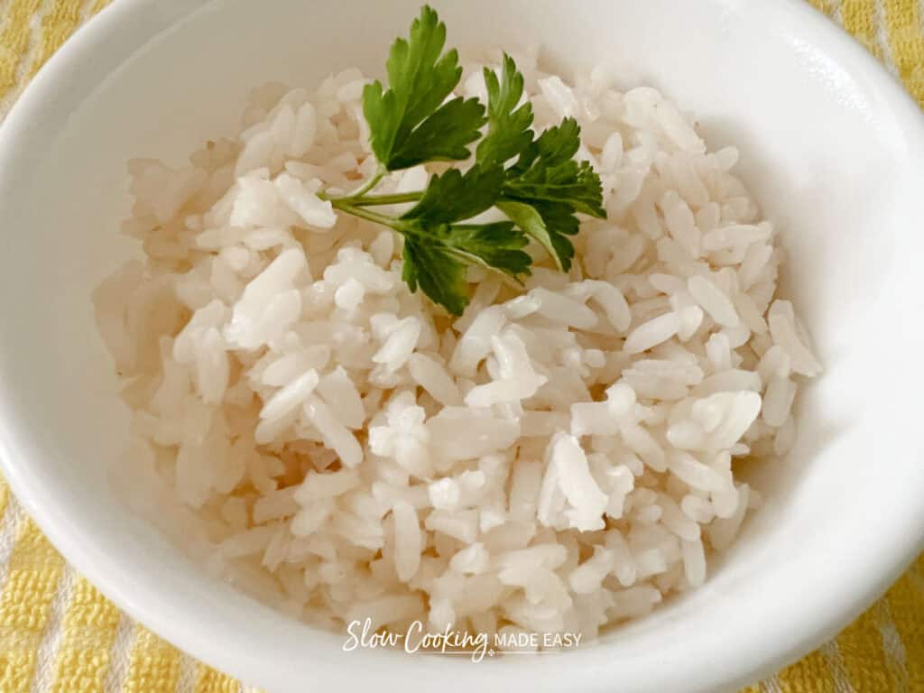 closeup of white rice in a bowl with a sprig of parsley