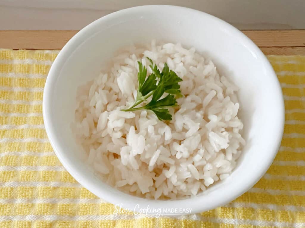 white rice in a bowl with a sprig of parsley on a yellow towel