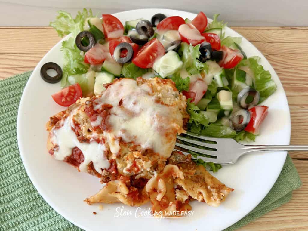 a plate with a piece of slow cooker lasagna and a salad and a fork