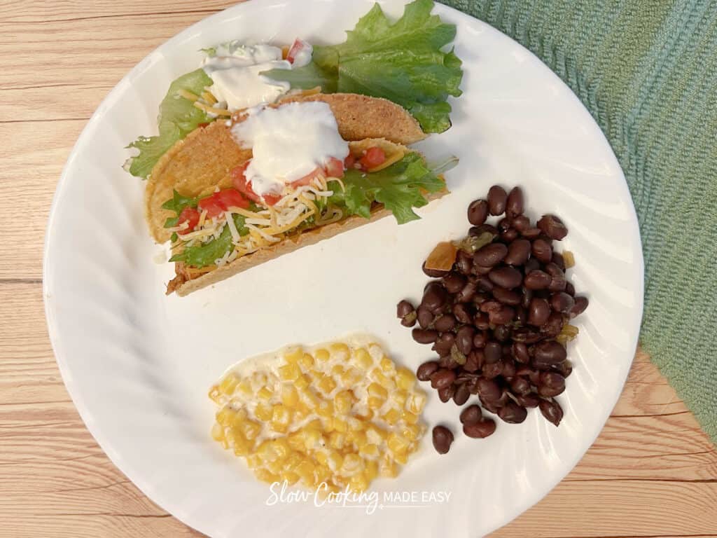 slow cooker bbq black beans on a plate with creamed corn, and two tacos