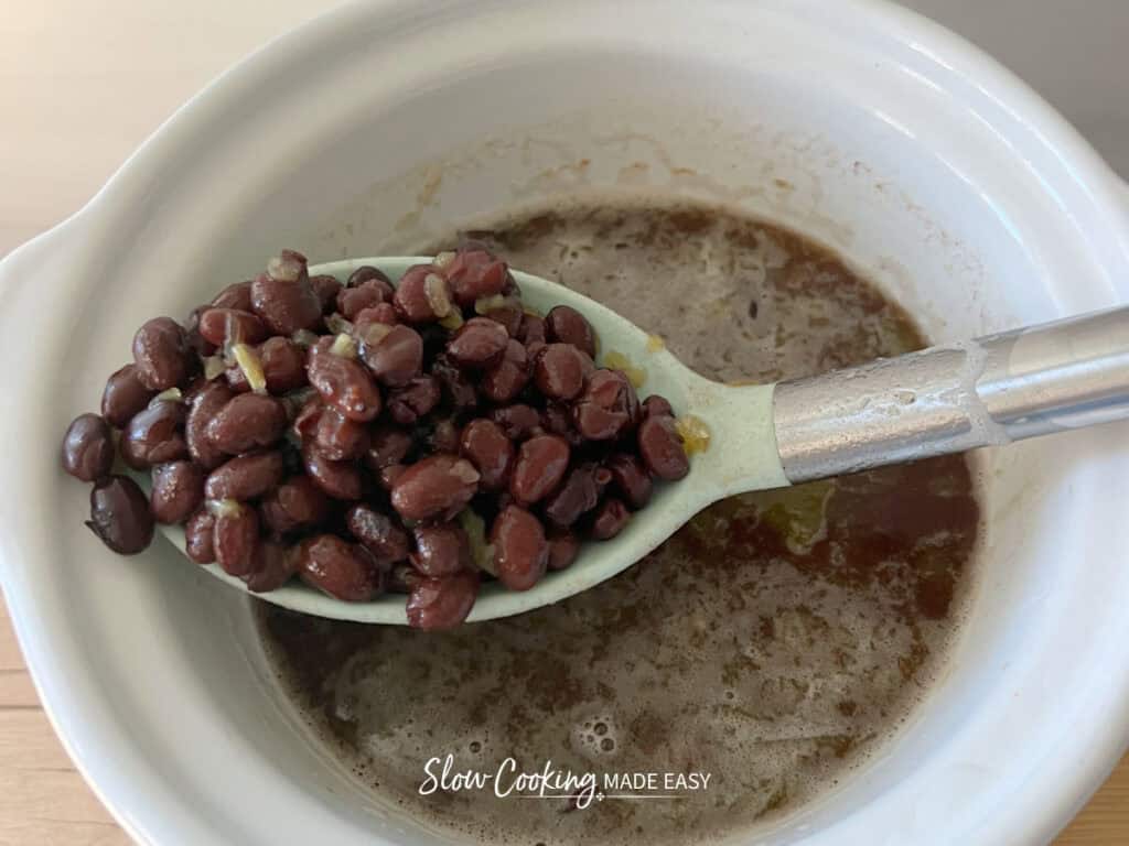 bbq black beans in a slow cooker with a spoonful of beans hovering above the rest