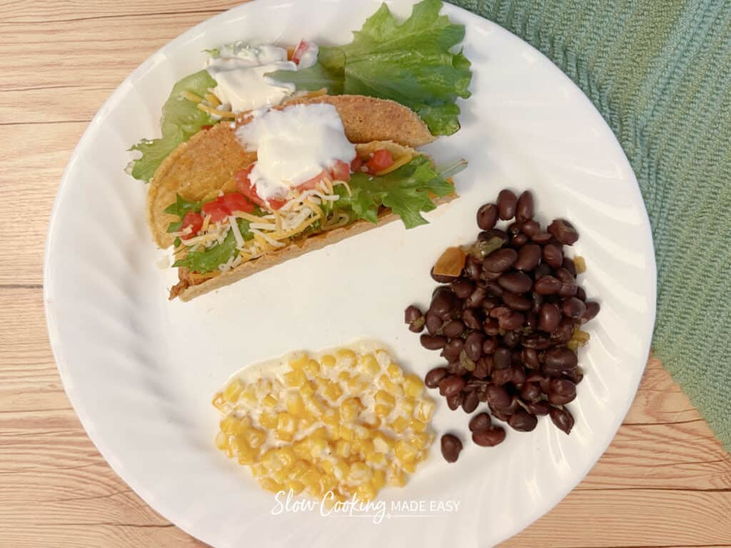 slow cooker creamed corn on a plate with black beans, and 2 tacos